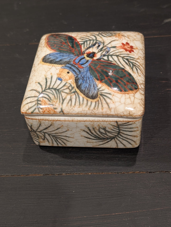 HomArt tropical porcelain keepsake box with colorful winged insect and palm frond design, angled view
