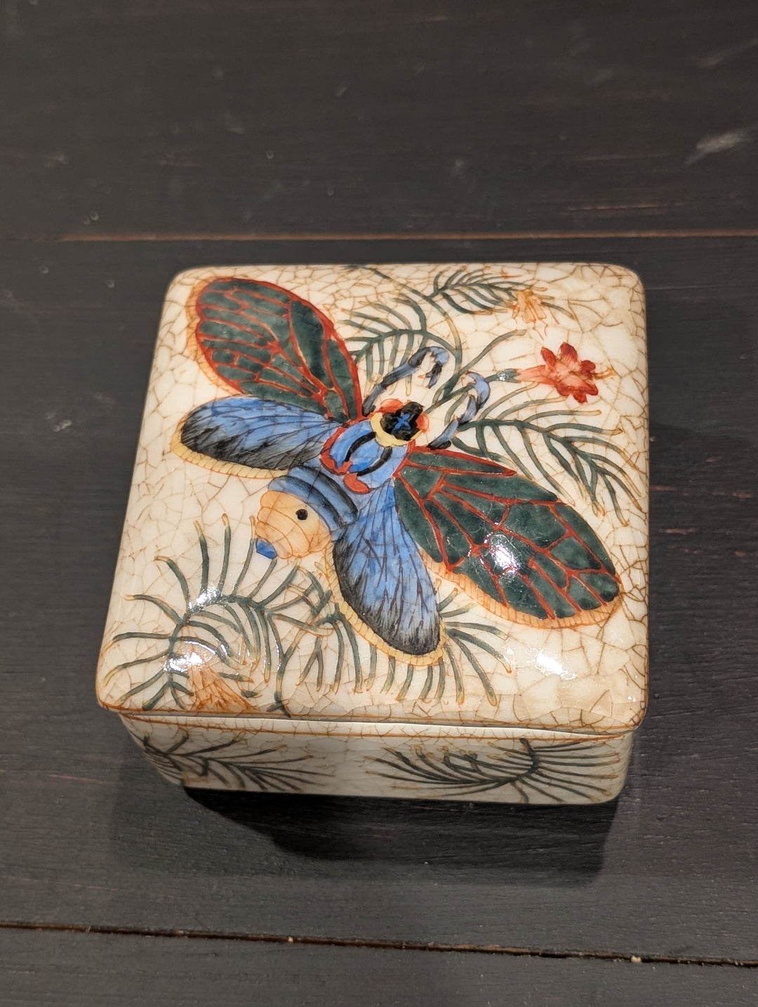 Top view of HomArt porcelain keepsake box lid with hand-painted tropical insect, palm fronds, and orange blossoms