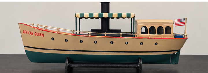 African Queen steamboat model with striped canopy, black funnel, cabin, and American flag on display stand