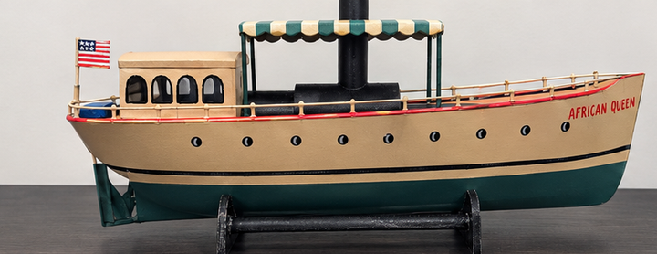 African Queen riverboat model in cream and green with red bow lettering on black stand